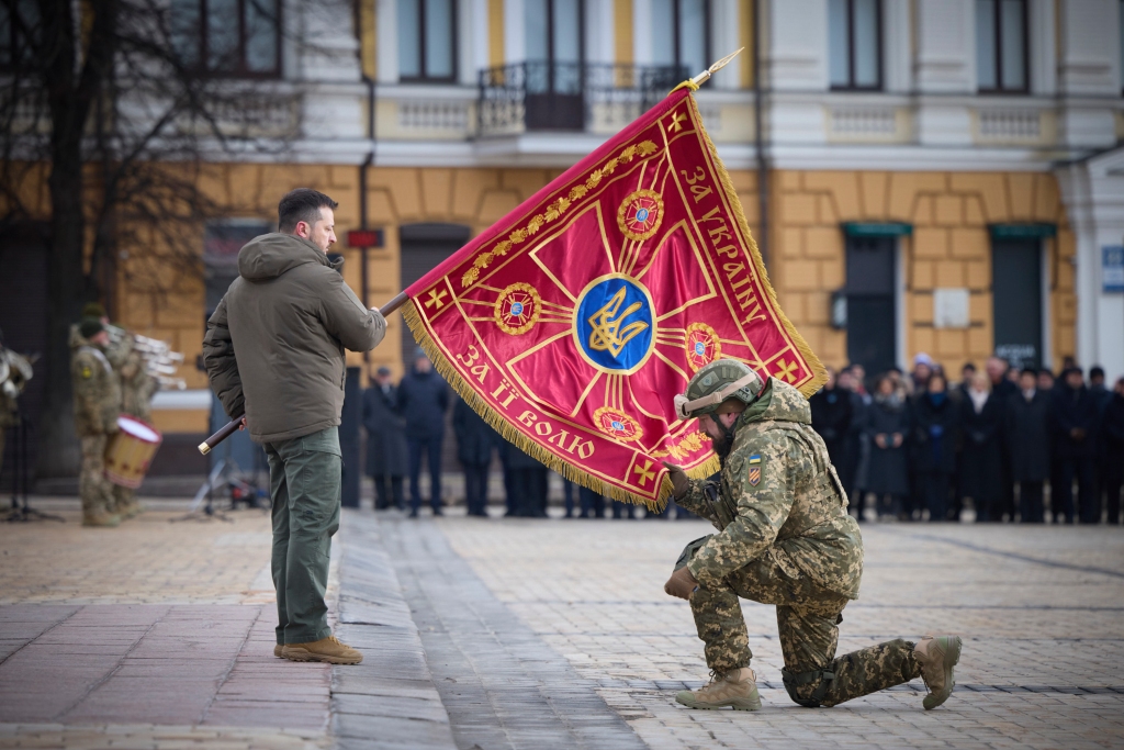 Ukrainian President Volodymyr Zelensky, left, holds the flag of a military unit as an officer kisses it, during commemorative event on the occasion of the Russia Ukraine war one year anniversary in Kyiv, Ukraine, Friday, Feb. 24, 2023. 