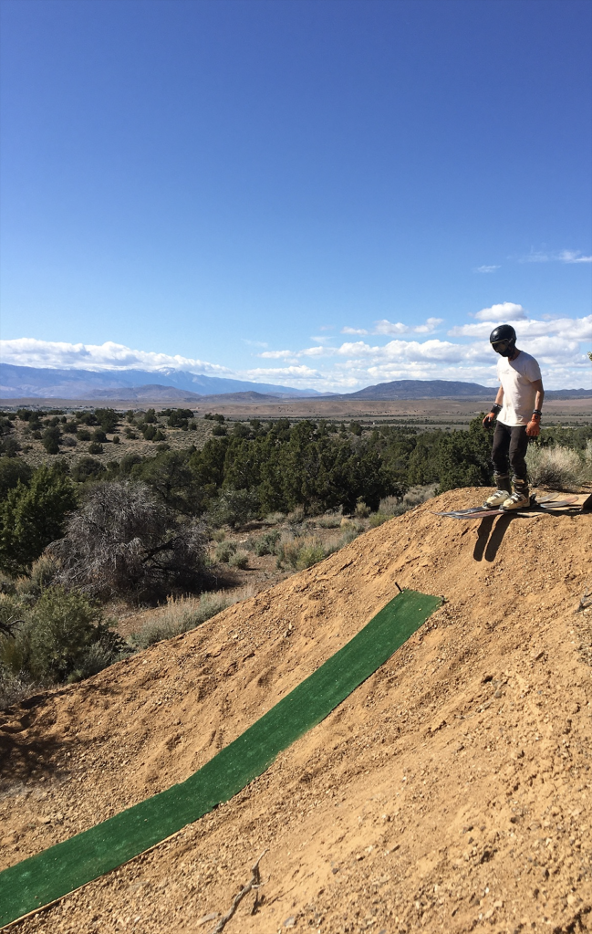 Man about to ski down dirt hill with makeshift equipment. 