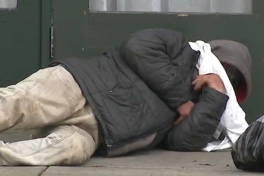 A homeless man sleeps in the street.