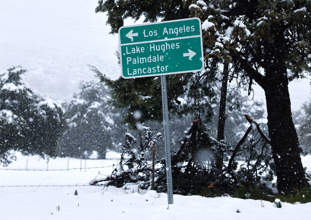 A sign points to Los Angeles as snow falls in Los Angeles County, in the Sierra Pelona Mountains, on February 25, 2023 in Green Valley, California. 