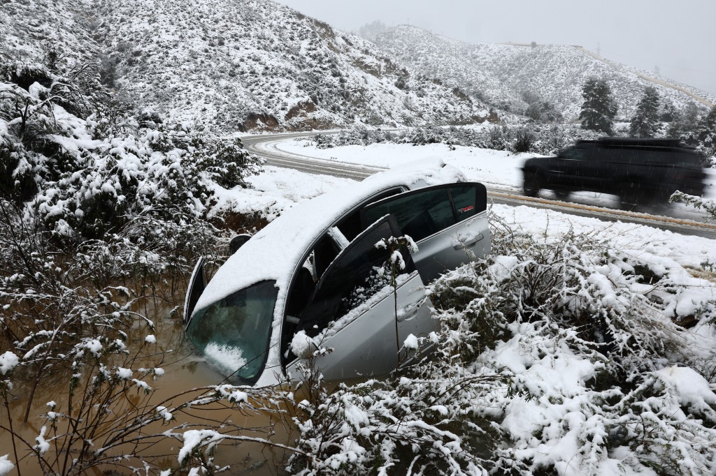 : A vehicle which skidded off the snowy roadway into a small pond earlier in the day is viewed in Los Angeles County, in the Sierra Pelona Mountains, on February 25, 2023 near Green Valley, California.