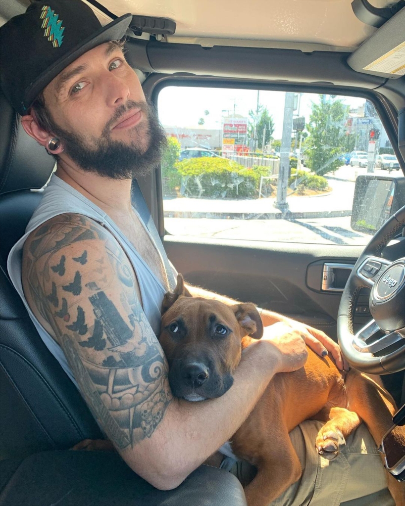 Navarone Garcia smiling sitting in a car with a dog on his lap. 