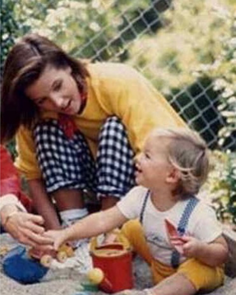 Lisa Marie Presley with her half brother, Navarone Garcia, when he was a toddler. She crouches over a toddler who smiles up at her. 