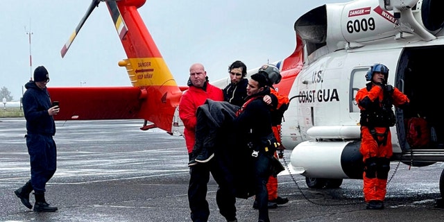 In this photo provided by the U.S Coast Guard Pacific Northwest, Coast Guard personnel help carry a swimmer from a rescue helicopter after he was rescued from the mouth of the Columbia River after his boat was capsized by a giant wave on Friday, Feb. 3, 2023, at Coast Guard Base Astoria, Oregon. 