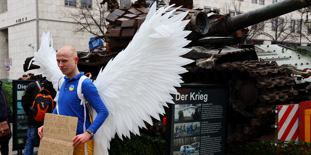 A protester holds a banner next to remains of a destroyed Russian T-72 tank in Berlin on Friday.