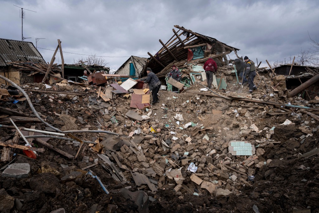 A resident of a house and their neighbors clear rubble from a home destroyed by a Russian rocket in Ukraine on Feb. 21, 2023.