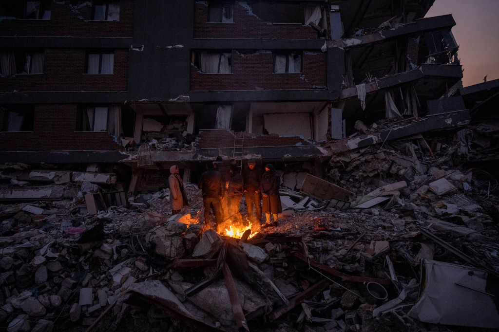 Members of the Aytulun family warm themselves around a campfire in front of the building where five members of their family were fatally trapped during the earthquake in Antakya, southeastern Turkey, Sunday, February 12, 2023. 