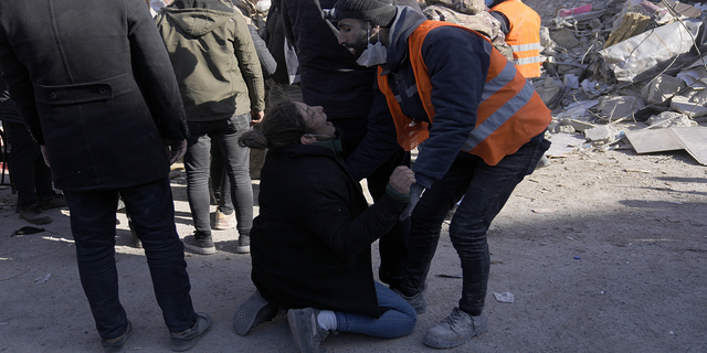 A woman cries as people stand in front of a destroyed building in Kahramanmaras, southeastern Turkey, on Monday, Feb. 13.