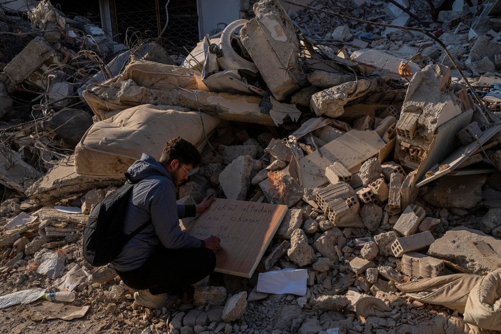 A man writes a text with contact details in case a body is retrieved under the rubble of a destroyed building in Antakya, southeastern Turkey, Monday, February 13, 2023.