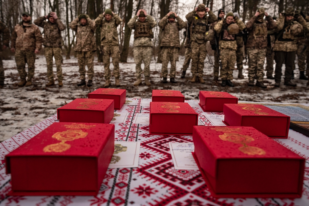 Medals sit on a table as Ukrainian servicemen of the Prince Roman the Great 14th Separate Mechanized Brigade adjust their hats before a flag ceremony where some of them were honored for their bravery and accomplishments in battle, in the Kharkiv area, Ukraine, Saturday, Feb. 25, 2023. 
