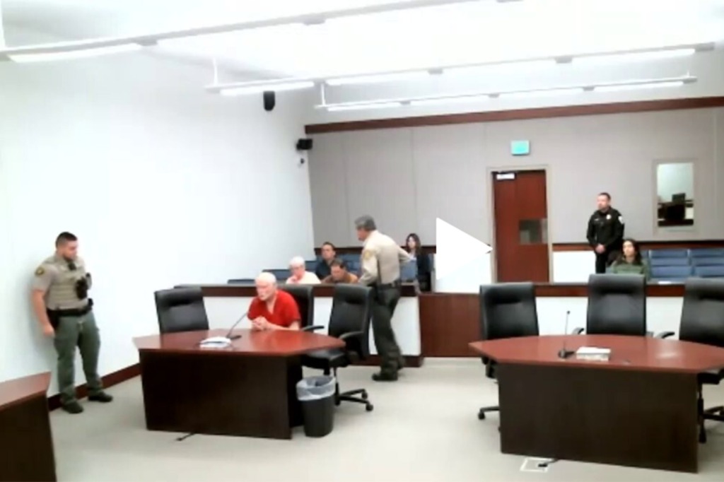 George Kelly sitting in an orange prison jumpsuit at a desk in a courtroom. 