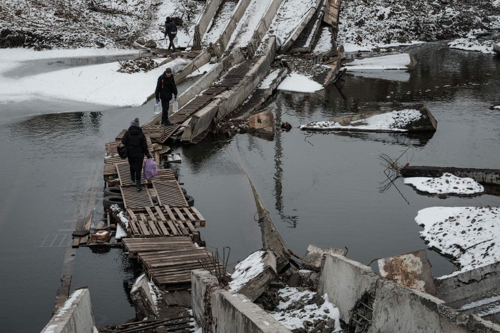 People walk on a destroyed bridge to cross a canal towards the disputed area in Bakhmut on February 1.