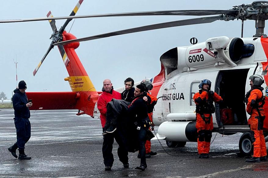 Coast Guard personnel help carry a swimmer from a rescue helicopter.