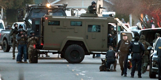 Law enforcement officers aim their weapons at a home during a standoff in Grants Pass, Ore., on Tuesday, Jan. 31, 2023. 