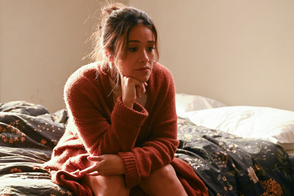 Gina Rodriguez in "Not Dead Yet" sits sulking on a bed. 