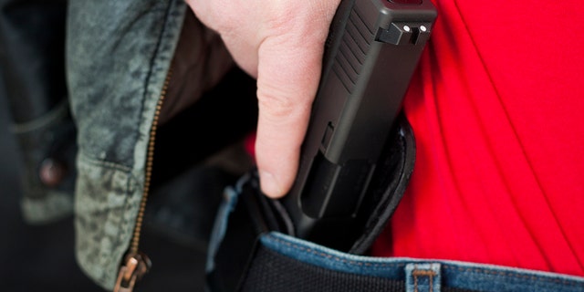 A man draws his Glock pistol from an inside-the-waistband holster.