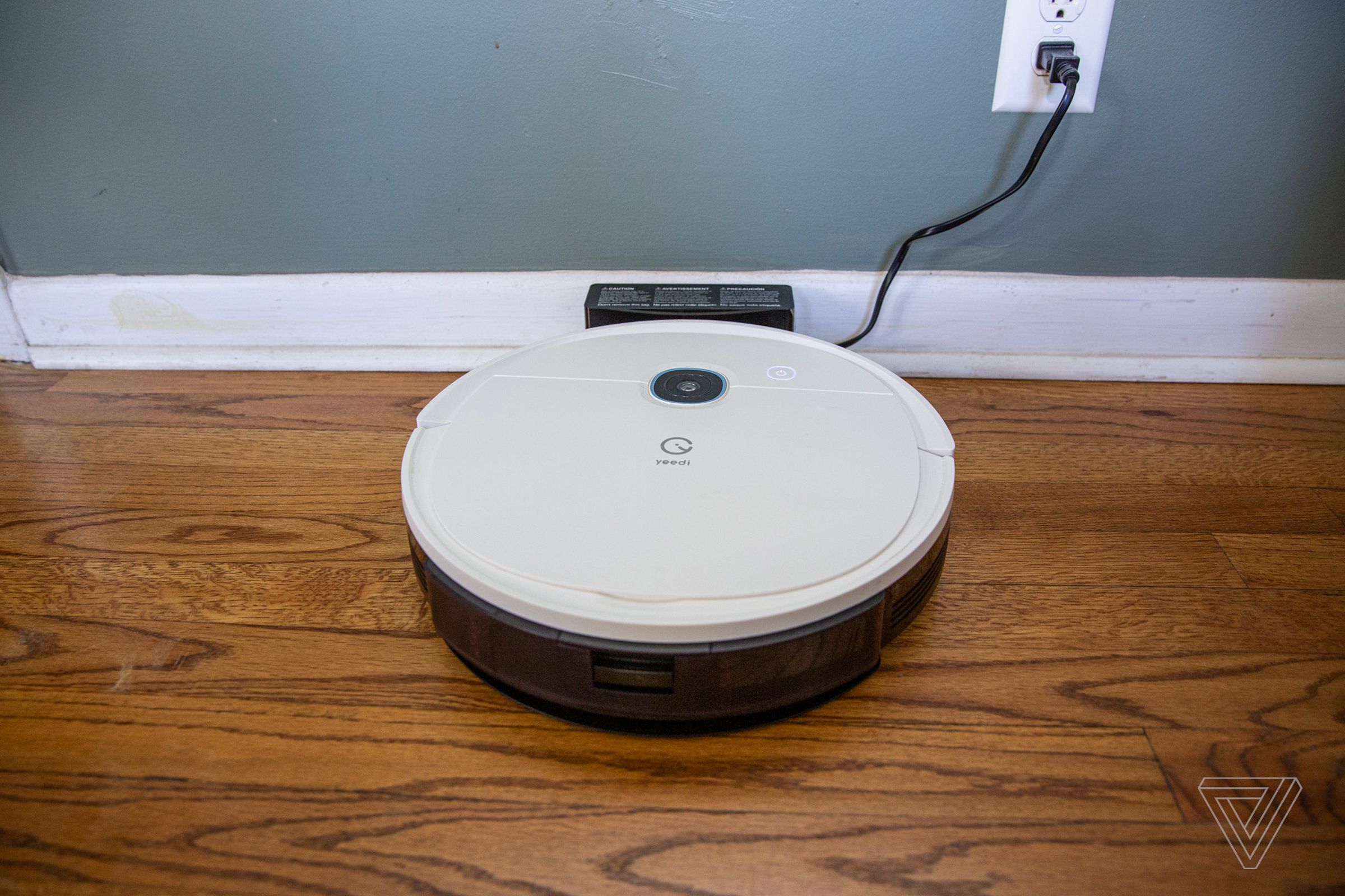 Yeedi’s Vac 2 Pro robot vacuum sitting on a hardwood floor charging against a wall.