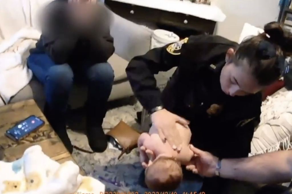 Officer Alexis Callaway administers the lifesaving technique on the choking infant, as family members nervously watch.