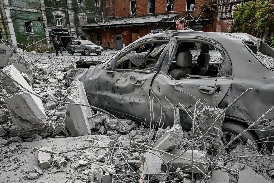 A woman stands near her destroyed car near an old mill.