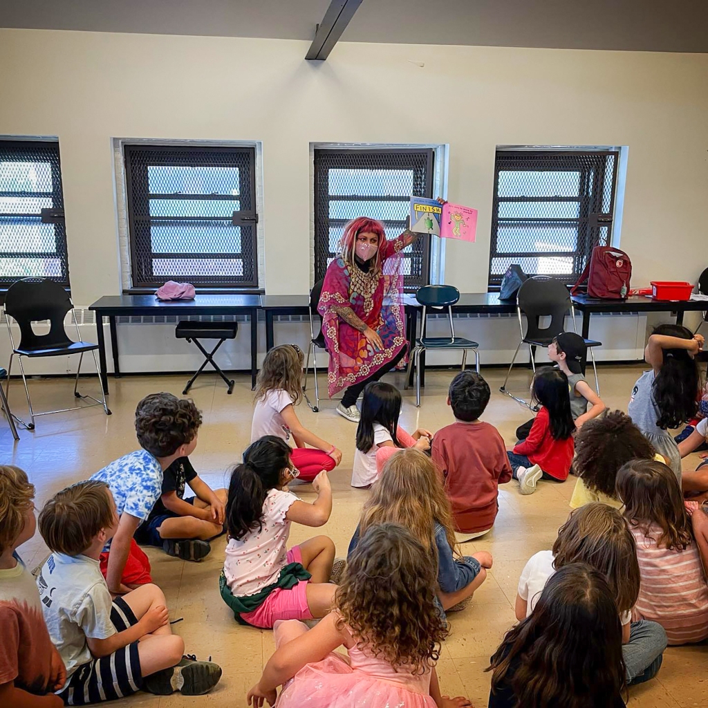 A picture of a drag queen reading books to children at a school.