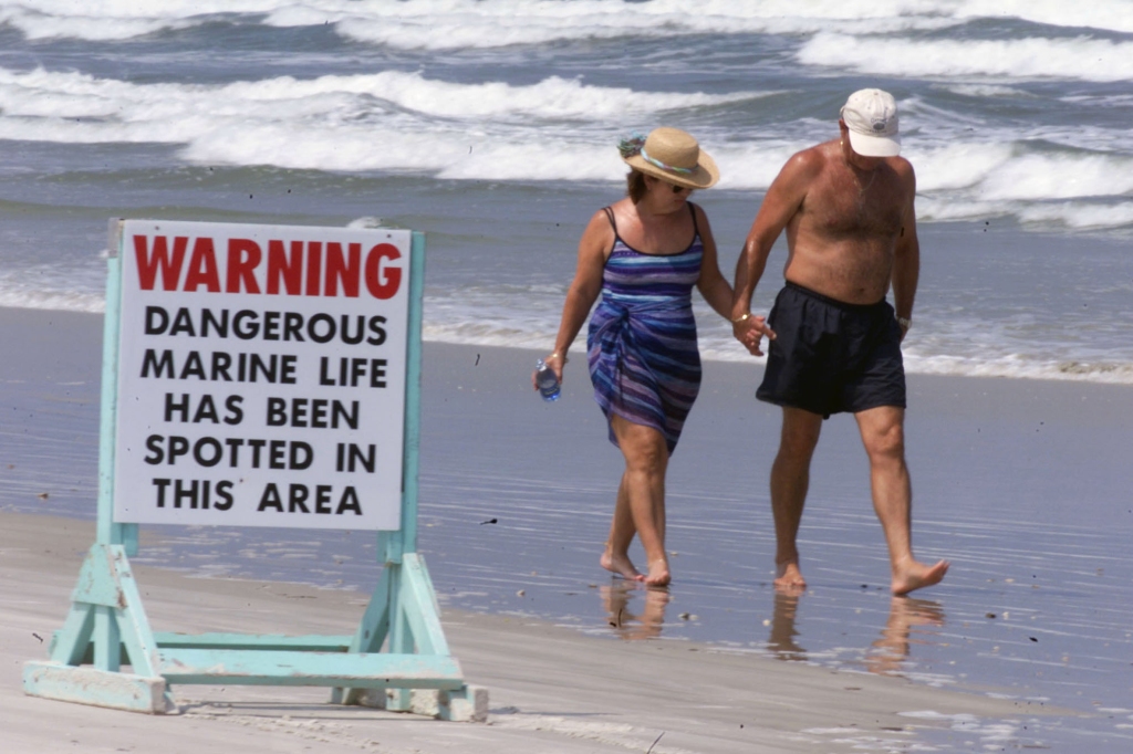 Florida beachgoers walk by a sign warning of sharks.