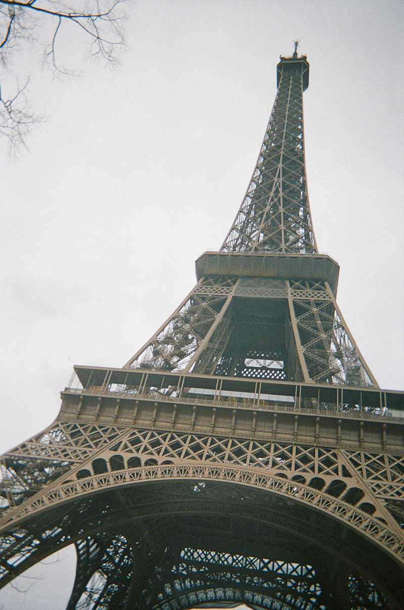 The intricately designed midsection of the Eiffel Tower, made of iron, stands out against a white sky.