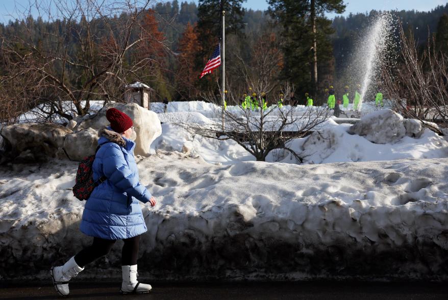 A pedestrian walks as members of the California Army National Guard Joint Task Force Rattlesnake shovel snow from a rooftop in Crestline, Calif.