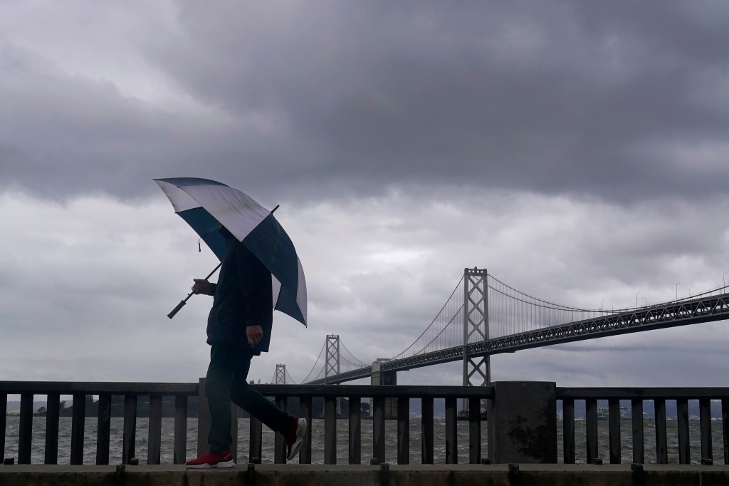 A pedestrian carries an umbrella while walking in front of the San Francisco-Oakland Bay Bridge in San Francisco, on March 21, 2023.