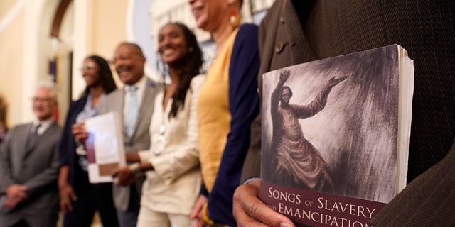 FILE — Dr. Amos C. Brown, Jr., vice chair for the California Reparations Task Force, right, holds a copy of the book Songs of Slavery and Emancipation, as he and other members of the task force pose for photos at the Capitol in Sacramento, Calif., on June 16, 2022.