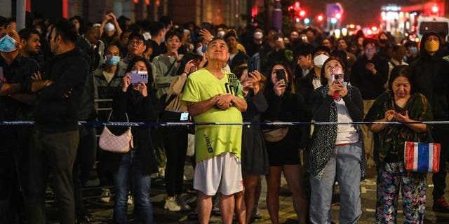 People watch as a fire burns at a high-rise building under construction in the Tsim Sha Tsui district in Hong Kong on March 3, 2023. 