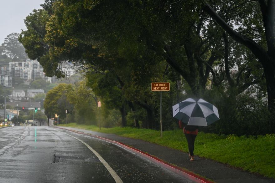 A woman walks with an umbrella on a sidewalk during heavy rain in San Francisco, Calif. on March 9, 2023.