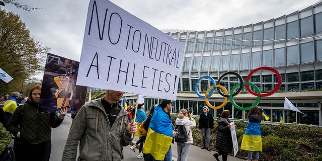 Ukrainians walk past the headquarters of International Olympic Committee (IOC) during a protest against the proposed IOC roadmap to organise the return to competition of Russian athletes under a neutral flag, provided that they have "not actively supported the war in Ukraine" in Lausanne on March 25, 2023. 