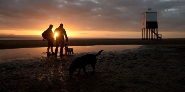 People photograph the S near to the lighthouse at Burnham-on-Sea, Somerset, as the sun sets an hour earlier after the clocks went back one hour last night due to the end of Daylight Saving Time.