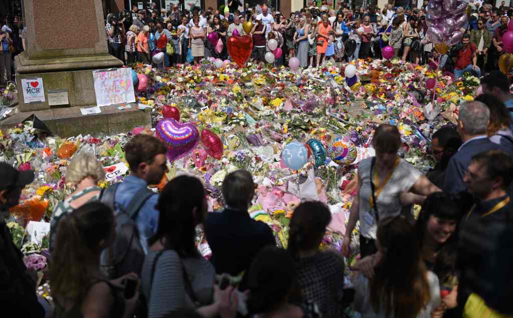 People stop by a mass of flowers to observe a minute's silence in St Ann's Square in Manchester, northwest England