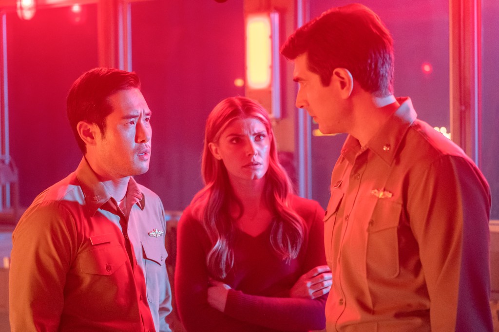 Raymond Lee, Caitlin Bassett, and Brandon Routh in "Quantum Leap" standing in a huddle talking in red lighting. 