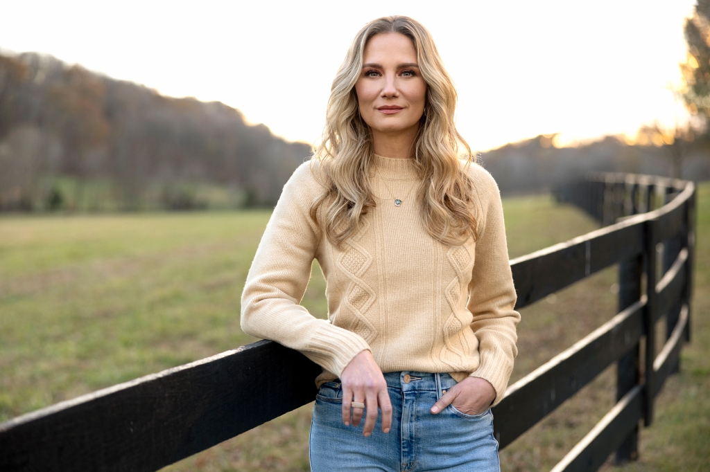 Jennifer Nettles leaning against a fence smiling. 