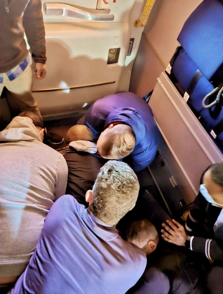 This image provided by Simik Ghookasian shows passengers and crew members restraining a man who according to federal authorities tried to open an airliner emergency door.
