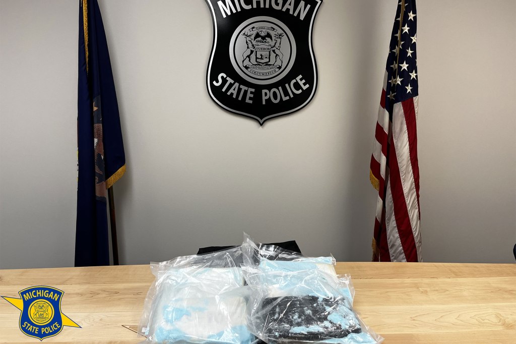Bags of blue pills sit on a desk in front of a wall with a Michigan State Police emblem