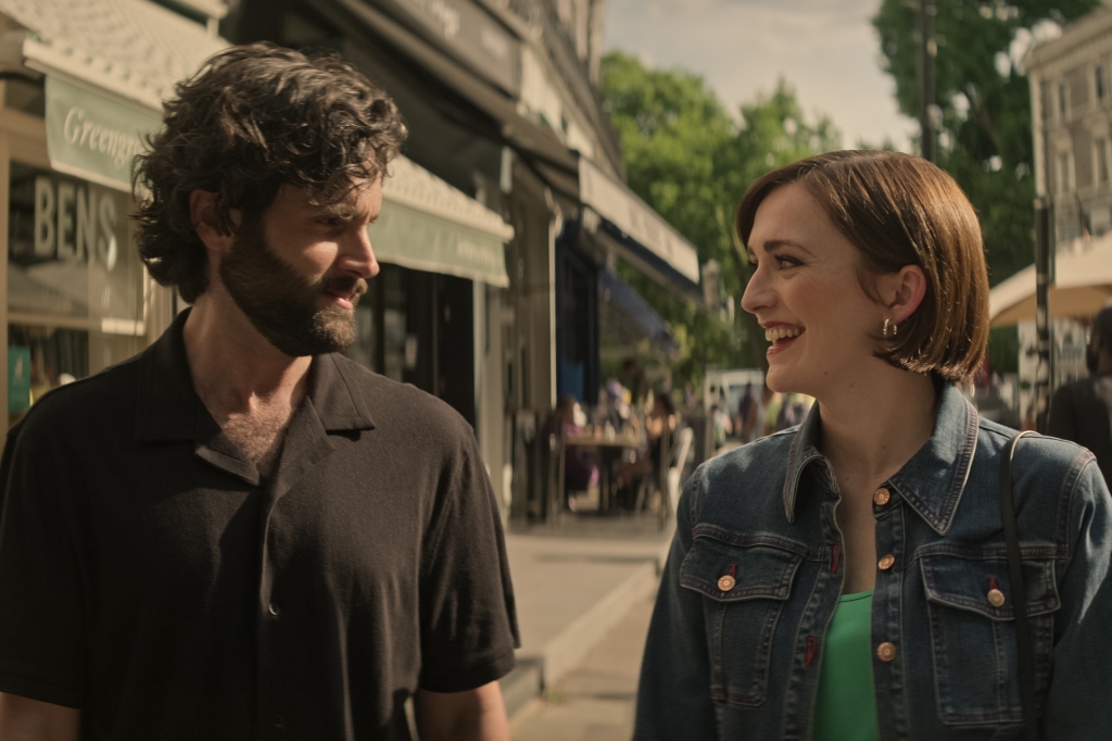 Joe (Penn Badgley) with Kate (Charlotte Ritchie) in "You" walking down a street smiling at each other. 