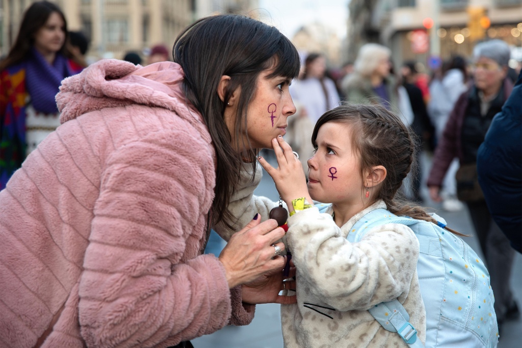 A girl paints the female symbol on an adult woman's face during a International Women's Day demonstration in Barcelona