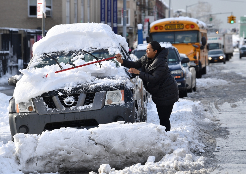 A woman is pictured removing snow from a car.