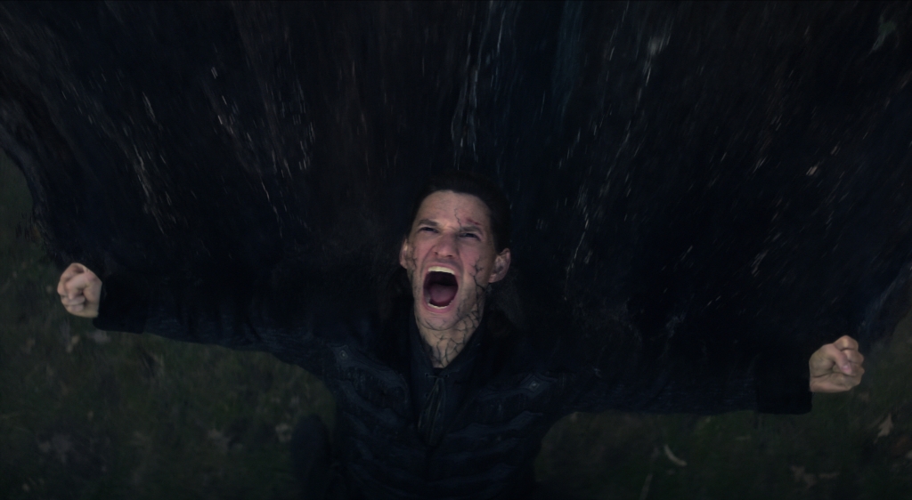 Ben Barnes grimacing and yelling at the sky with his arms out, at night. 