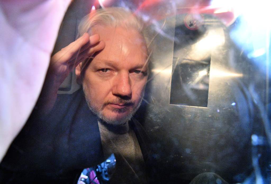  Assange gestures from the window of a prison van as he is driven out of a London court on May 1, 2019, after having been sentenced to 50 weeks in prison for breaching his bail conditions in 2012