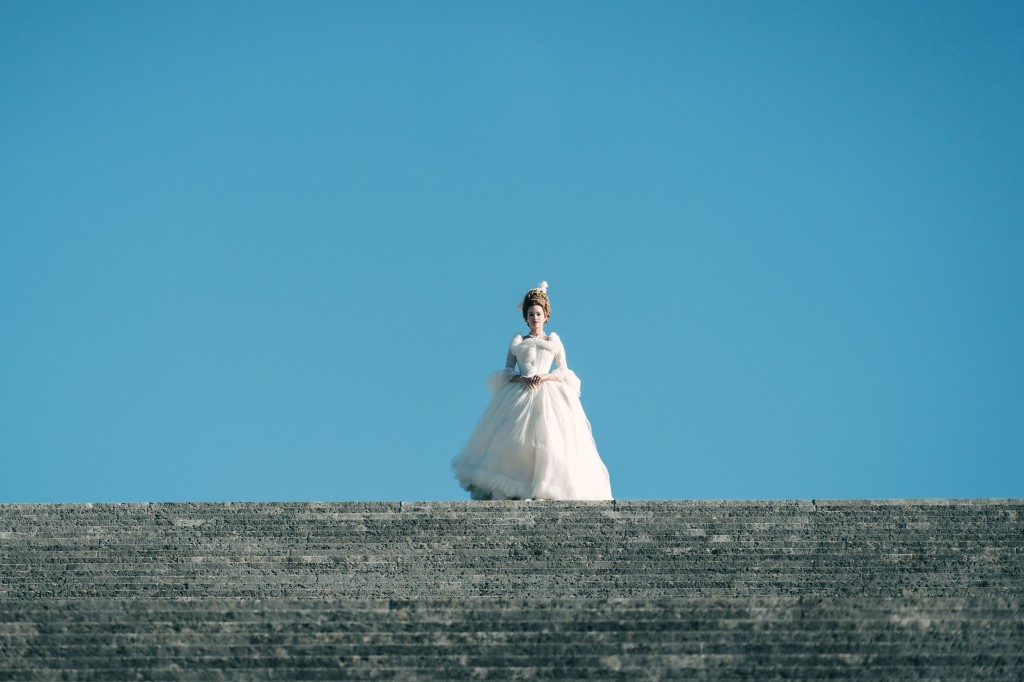 Emilia Schüle in "Marie Antoinette" standing outside in a puffy dress. 