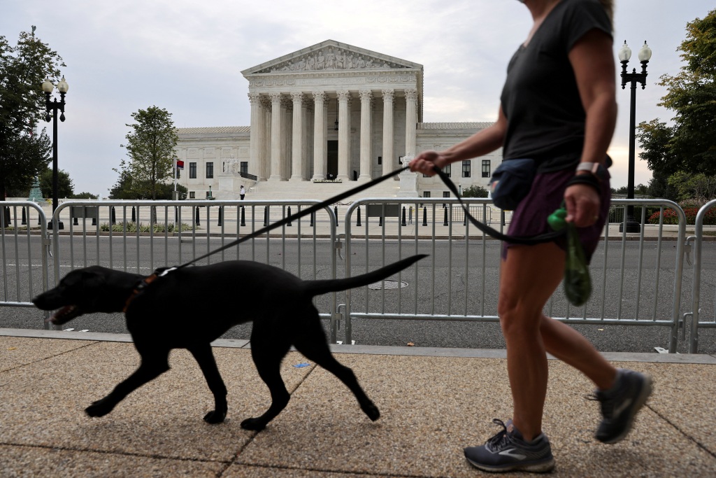 A woman walks a dog on a sidewalk across the street from the U.S. Supreme Court.