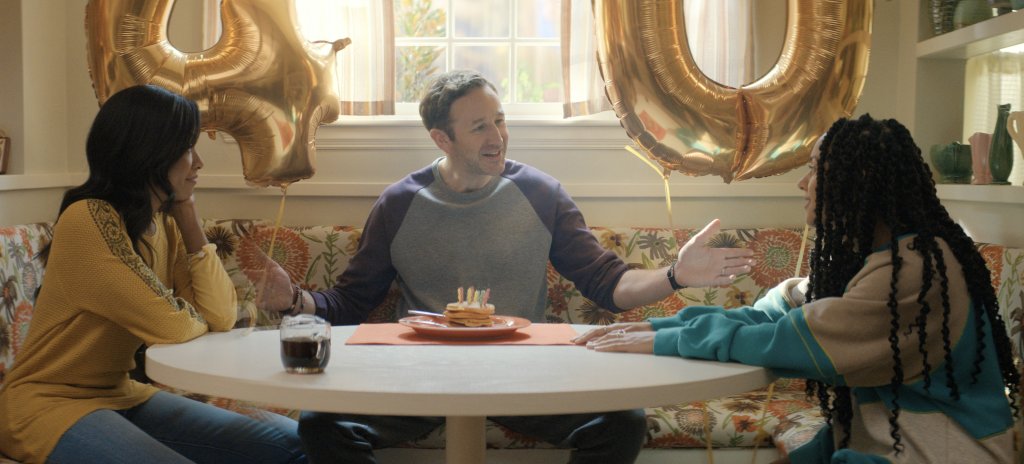 Dusty (Chris O'Dowd) with his wife Cass (Gabrielle Dennis, left), and his daughter, Trina (Djouliet Amara, right) sitting together having breakfast. 