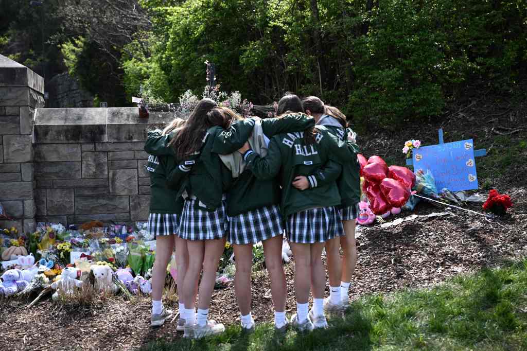 Girls embrace in front of a makeshift memorial for victims by the Covenant School building at the Covenant Presbyterian Church.