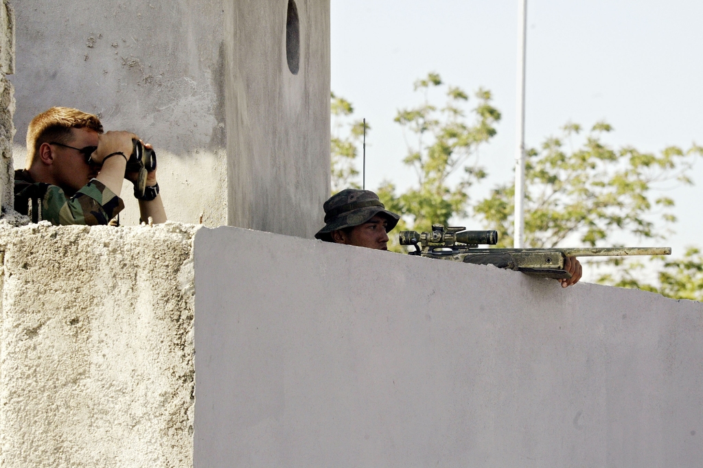 A United States Marine scout sniper and his spotter keep watch above a gate at the industrial park March 12, 2004 in Port-au-Prince, Haiti. 