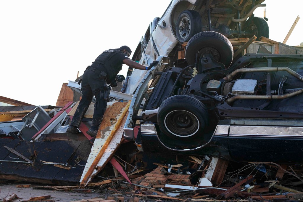 A sheriff's deputy climbs onto a pile of wind-tossed vehicles to search for survivors or the deceased at Chuck's Dairy Bar in Rolling Fork, Miss., Saturday, March 25, 2023.