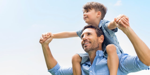 Portrait of happy father giving son piggyback ride on his shoulders and looking up.